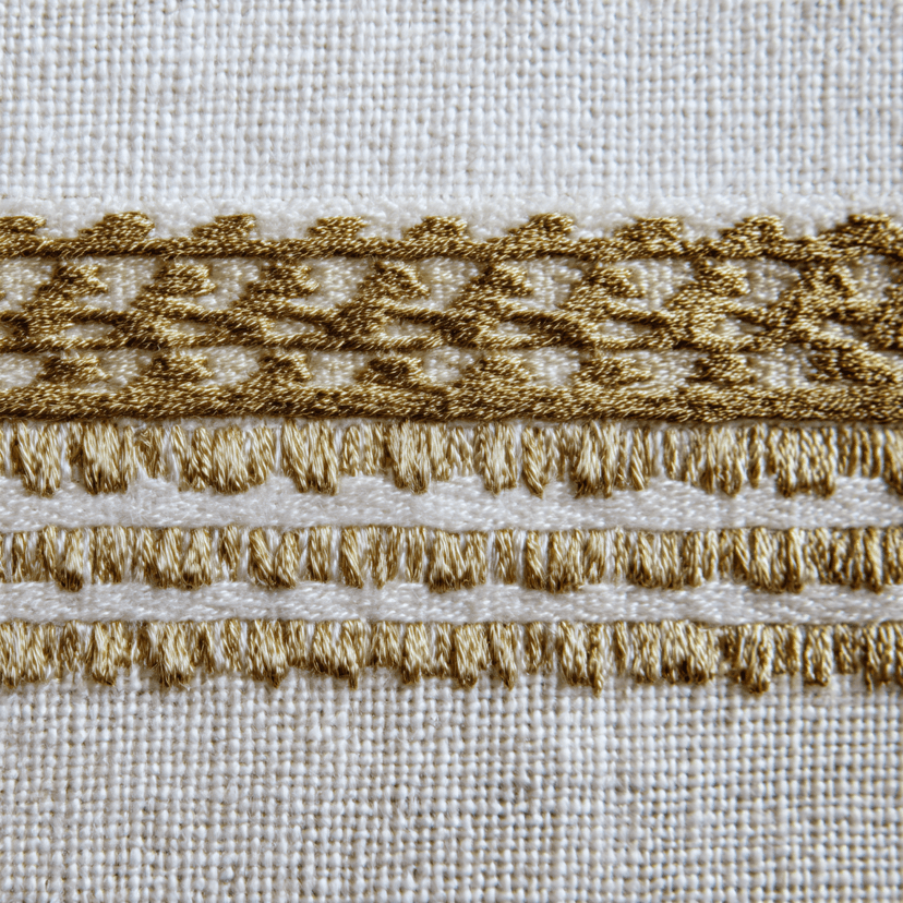 Extreme macro close-up of a Menen-style woven netela border showing gold metallic supplementary weft threads interlaced into white hand-spun cotton, geometric diamond pattern visible