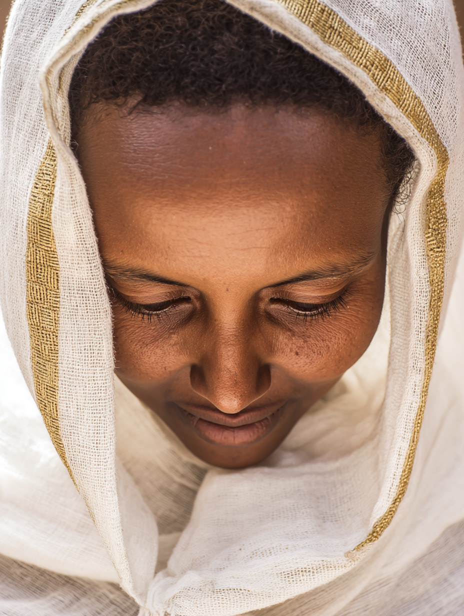 Close-up portrait of Ethiopian woman with white netela pulled over her head as a church head covering, gold tibeb border framing her face, soft natural light