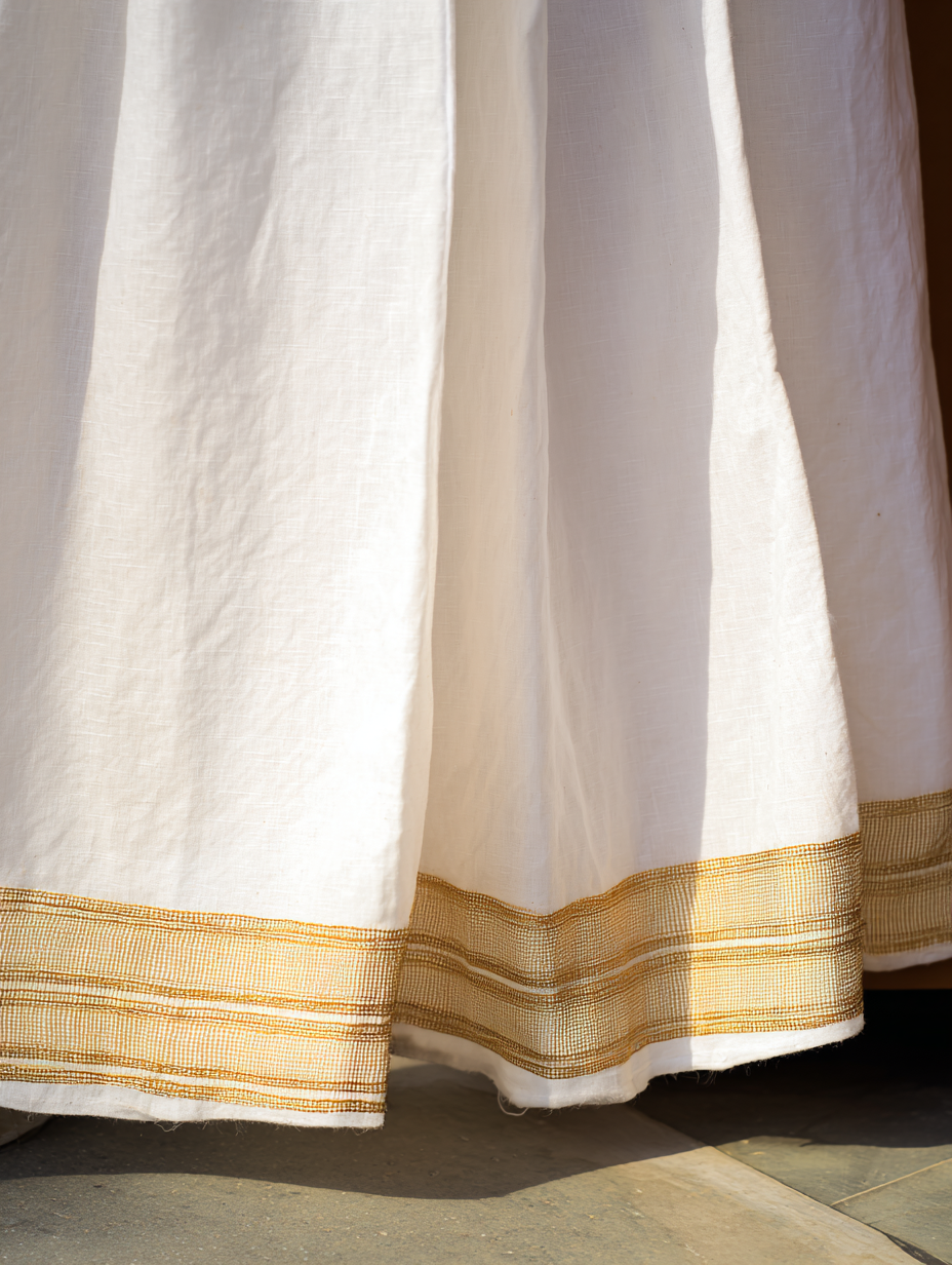 Close-up of a white habesha kemis hem showing a hand-woven gold tibeb border with clean geometric pattern and raised thread texture against natural hand-spun cotton